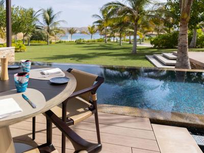 Terrazza con tavolo da pranzo e piscina con vista su giardino paesaggistico e mare.