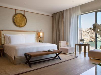 Lichte hotelkamer met kingsize bed, bankje, zitgedeelte en groot raam met uitzicht op landschap.