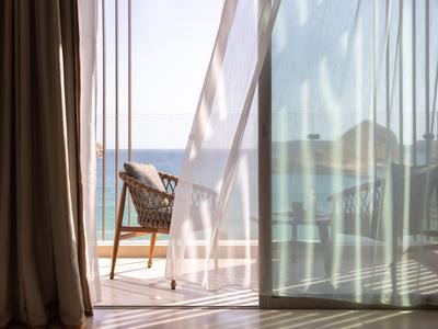 Porta del balcon aperta con vista sul mare e sedia sul balcone dietro una tenda trasparente