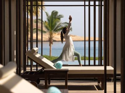 Donna in abito bianco che fa yoga su una terrazza con vista sul mare e sulle palme.