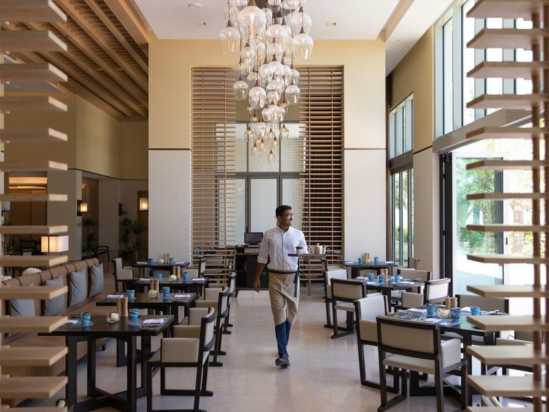 Modern hotelrestaurant met houten decor, grote ramen en een ober die loopt.