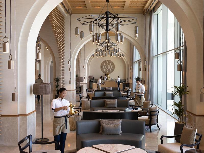 Ruime hotel lounge met hoge bogen, houten plafond, moderne zitplaatsen en grote ramen.