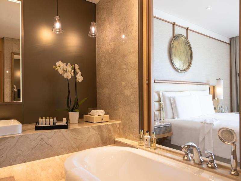 Modern hotelbadkamer met bad, spiegel, bloemen en warm licht.