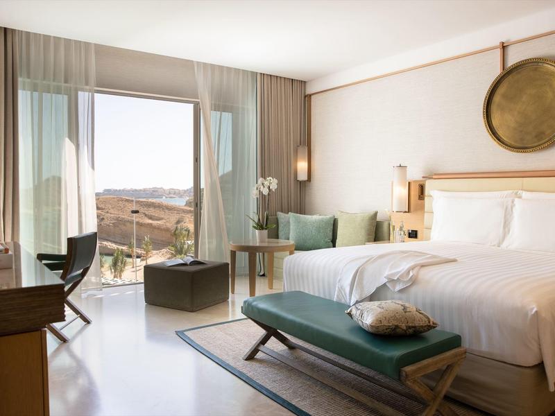 Lichte hotelkamer met tweepersoonsbed, balkonzicht en moderne houten en groene accenten.