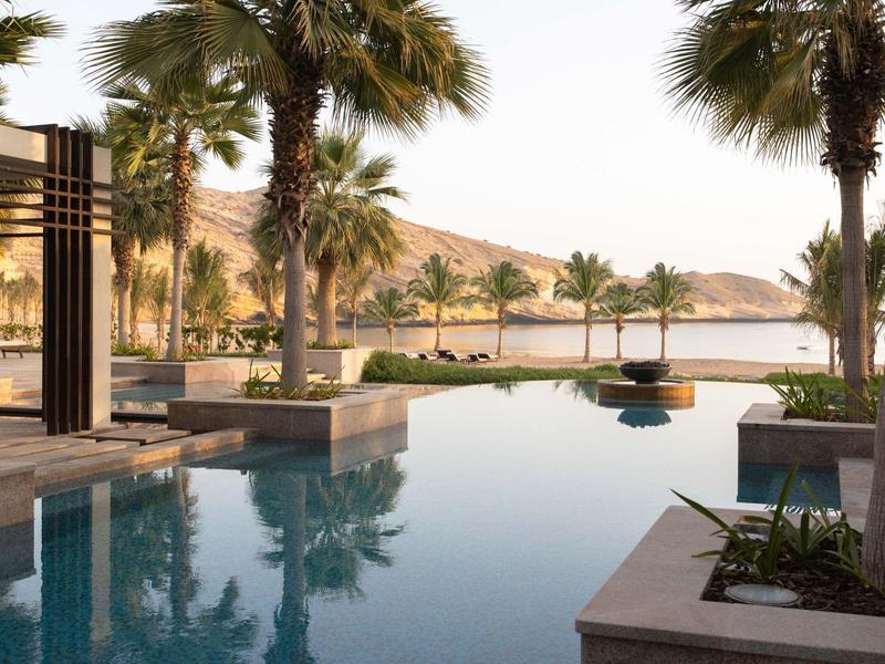 Luxe buitenzwembad omgeven door palmbomen met uitzicht op bergen bij zonsondergang.