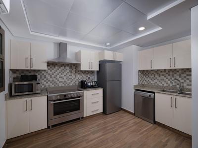 Modern hotel kitchen with white cabinets, stainless steel appliances, and wood flooring.
