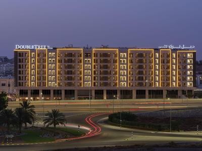 Modern illuminated hotel building at dusk with clearly defined balconies and palm trees in front.