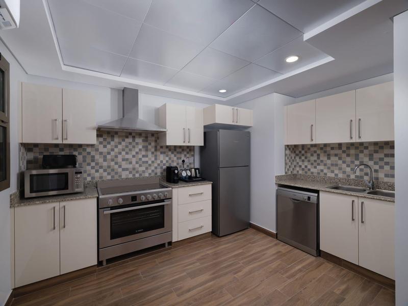 Modern hotel kitchen with white cabinets, stainless steel appliances, and wood flooring.