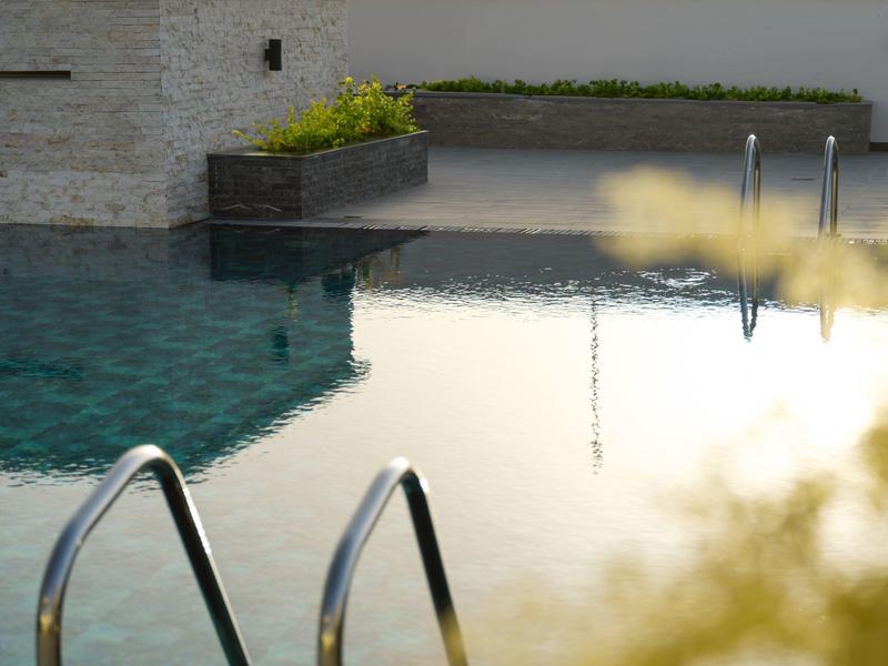 Modern outdoor pool with clear water and metal ladders, surrounded by a light stone wall.