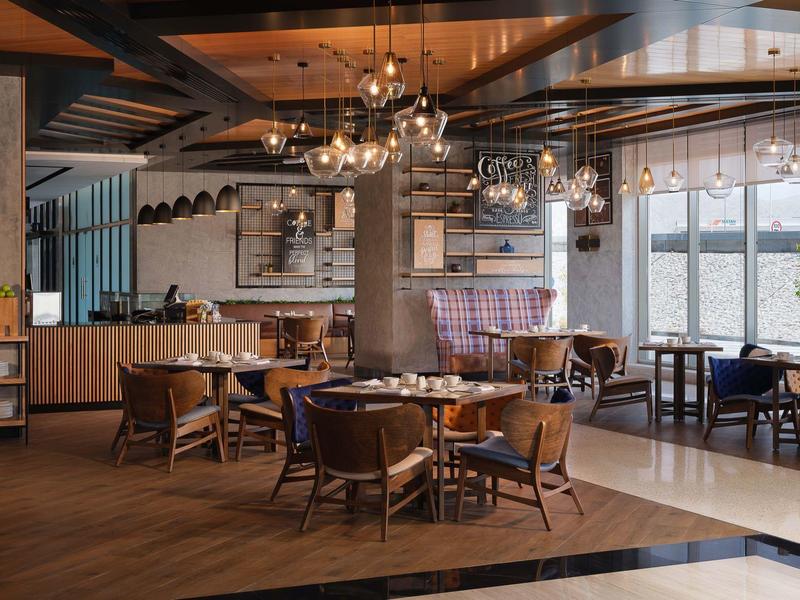 Cozy hotel dining area with wooden tables, leather chairs, and modern chandeliers.