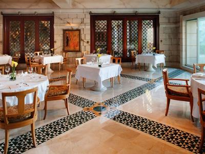 Eleganter Speisesaal mit runden Tischen, weißen Tischdecken, Holzstühlen und großen Fenstern.