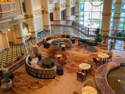 Amplia zona de descanso en hotel con sillones coloridos, mesas y suelo de mosaico.