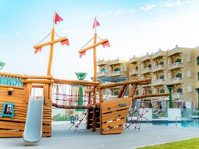Área de juegos infantil con barco pirata en el jardín de un hotel bajo cielo despejado