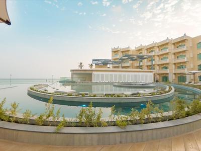 Complejo hotelero moderno con piscina redonda frente al edificio y vista al mar con cielo despejado.