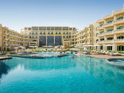 Gran hotel de varios pisos con una gran piscina azul en el patio.