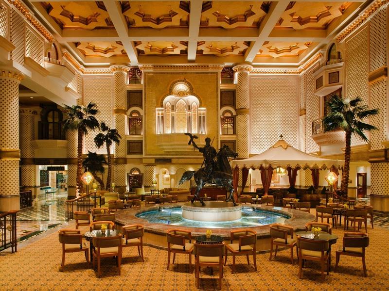Amplio interior con fuente central, estatuas y áreas de descanso en hotel con iluminación cálida.