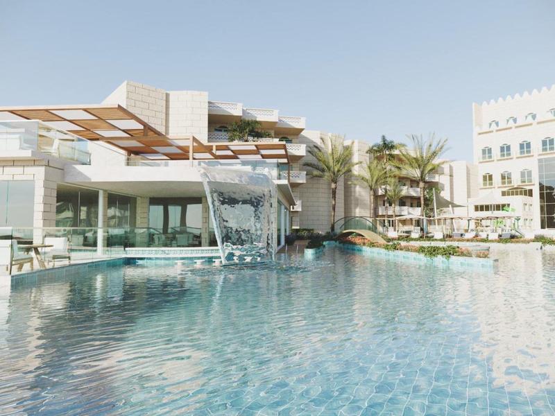 Piscina moderna de hotel con cascada y palmeras bajo un cielo despejado.