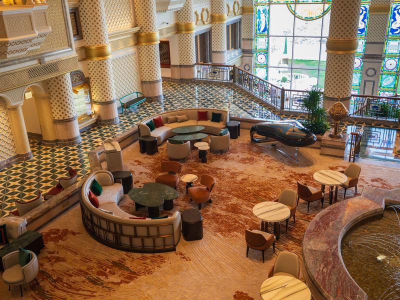 Amplia zona de descanso en hotel con sillones coloridos, mesas y suelo de mosaico.