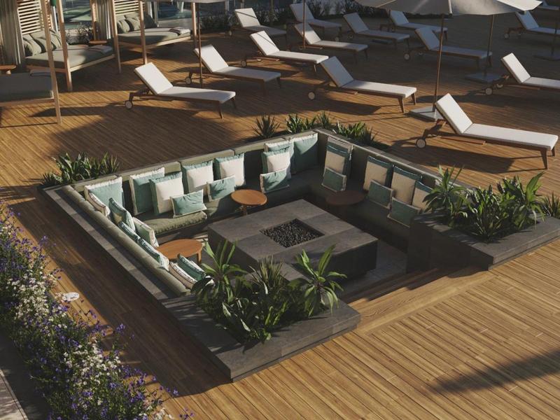 Área lounge moderna al aire libre con cojines, plantas y tumbonas sobre terraza de madera.