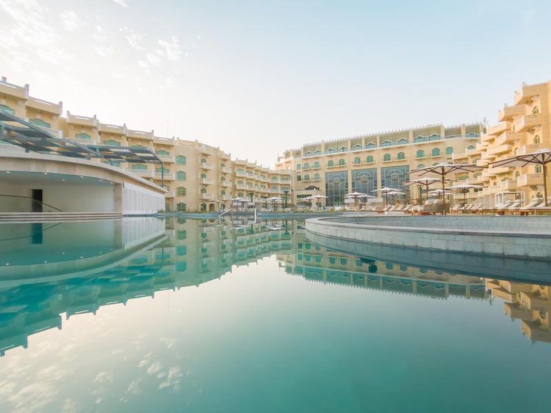 Gran piscina rodeada de edificios de hotel de varios pisos bajo un cielo despejado.