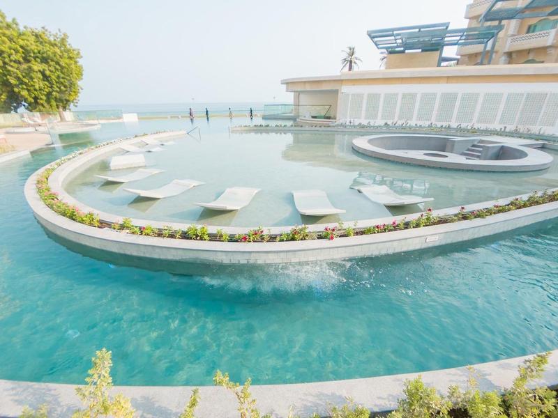 Piscina exterior moderna en forma de semicírculo con tumbonas y jacuzzi, vista al mar al fondo.