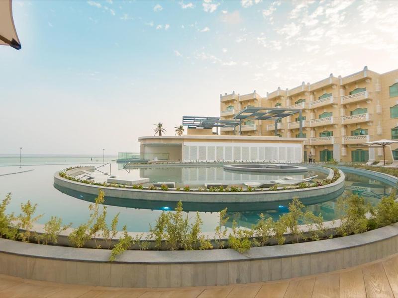 Complejo hotelero moderno con piscina redonda frente al edificio y vista al mar con cielo despejado.