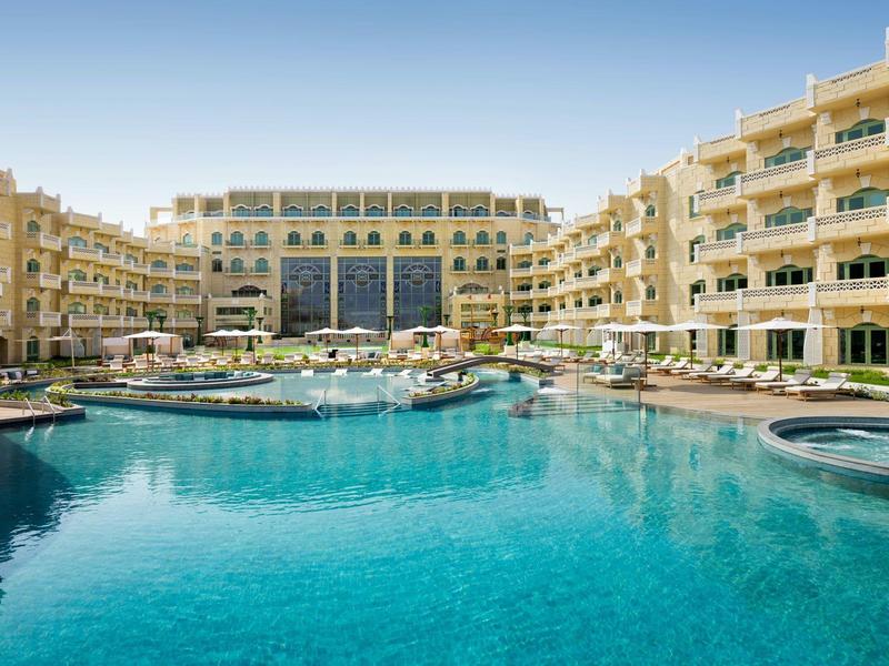 Gran hotel de varios pisos con una gran piscina azul en el patio.