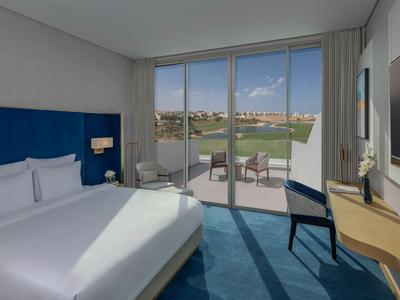 Modernes Hotelzimmer mit Doppelbett, Schreibtisch und Blick auf eine Terrasse mit Sitzgelegenheiten.