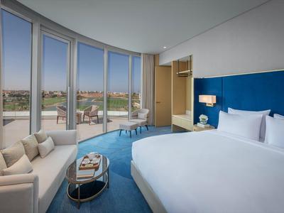 Modernes Hotelzimmer mit großem Bett, blauer Akzentwand und Panoramafenstern mit Stadtblick.