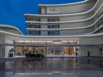Modernes Hotel mit geschwungenen Balkonen und reflektierendem Wasserbecken am Eingang bei Nacht.