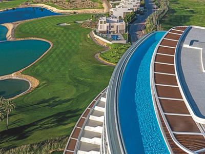 Blick auf ein Hotel mit Außenpool und Golfplatz in einer grünen Landschaft.