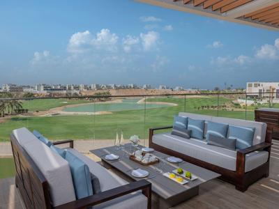 Moderne Terrasse mit Sofas und Tisch mit Getränken, Blick auf Golfplatz und Stadt im Hintergrund.