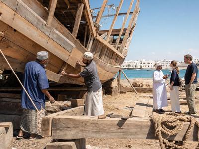 Männer reparieren ein großes Holzschiff am Hafen bei klarem Himmel.