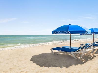 Leerer Sandstrand mit blauen Sonnenschirmen und Liegestühlen unter klarem Himmel
