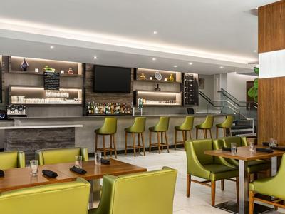 Moderne Hotelbar mit grünen Barhockern und Sesseln, Holz- und Steinelementen im Innenraum