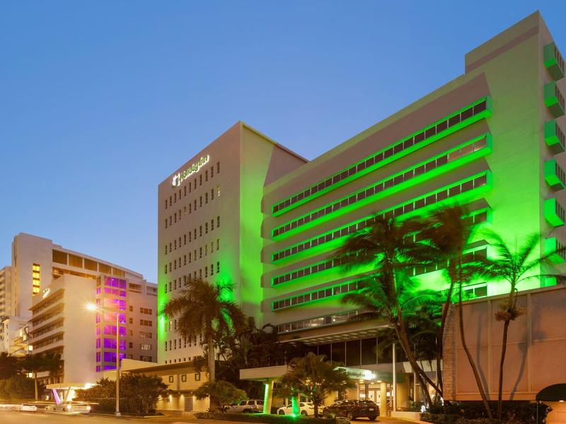 Budynek hotelu o zmierzchu z zielonym oświetleniem i palmami na pierwszym planie.