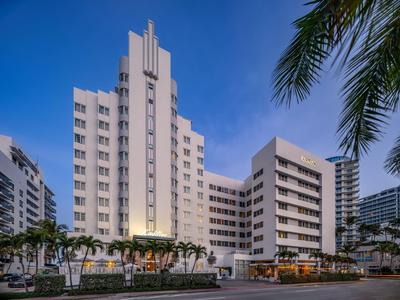 Hohes weißes Gebäude mit vielen Fenstern, Palmen im Vordergrund und blauem Himmel.