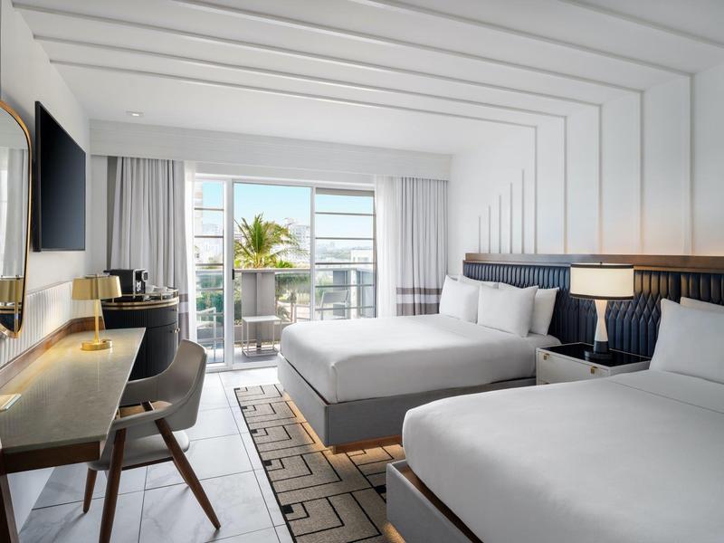 Modernes Hotelzimmer mit zwei großen Betten, Schreibtisch, Fernseher und Balkon mit Meerblick.