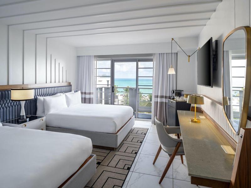 Modernes Hotelzimmer mit zwei Queensize-Betten, Schreibtisch, großem Spiegel und Meerblick durch Balkonfenster.