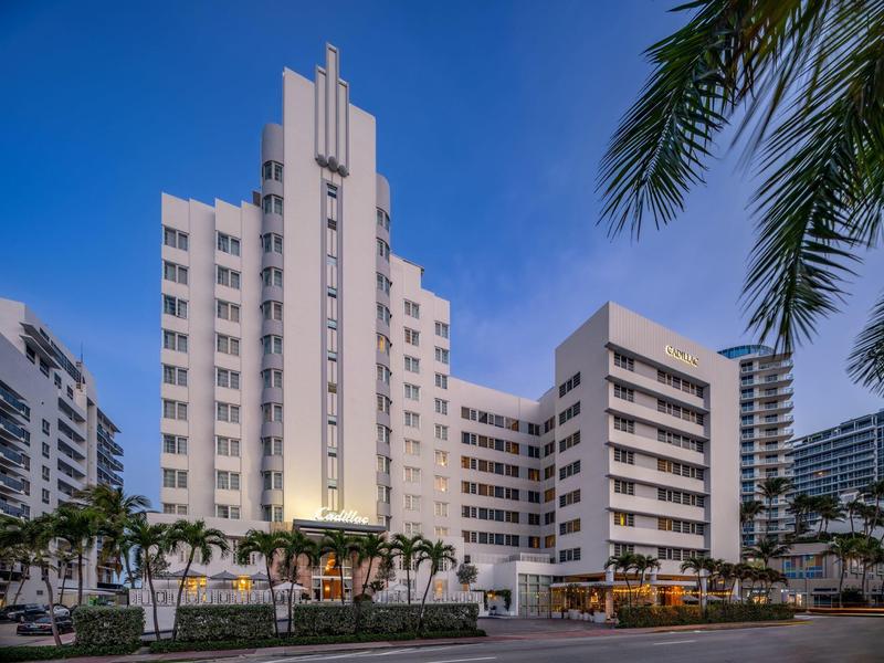 Hohes weißes Gebäude mit vielen Fenstern, Palmen im Vordergrund und blauem Himmel.