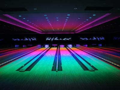 Leere Bowlingbahnen mit buntem Neonlicht in einer dunklen Halle.
