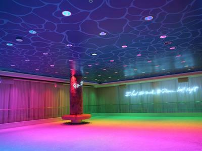 Farbig beleuchteter Innenraum mit einer Säule und einer beleuchteten Schrift an der Wand