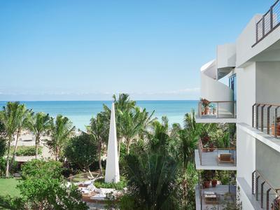 Blick auf grüne Palmen, weißen Sandstrand und blauen Ozean neben modernem Gebäude mit Balkon.