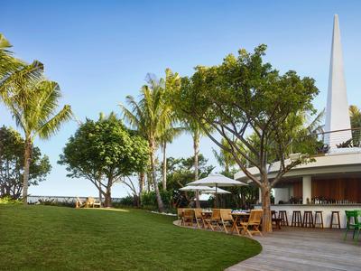Grüner Gartenbereich mit Stühlen und Sonnenschirmen neben einem Gebäude unter blauem Himmel