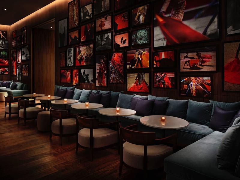 Gemütliche Bar mit runden Tischen, blauen Sofas und roten Bildern an dunklen Wänden.