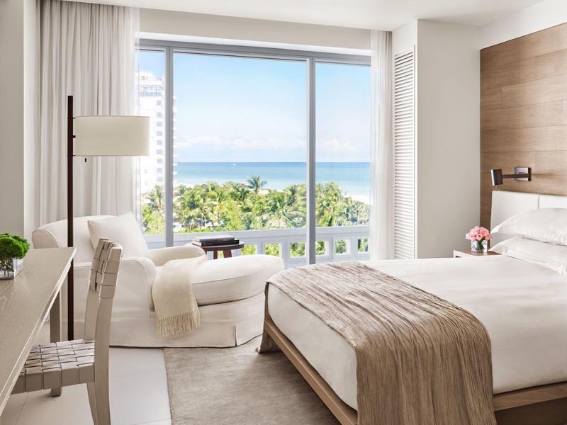 Helles Schlafzimmer mit großem Fenster, Doppelbett mit braunem Überwurf, Sessel und Schreibtisch.