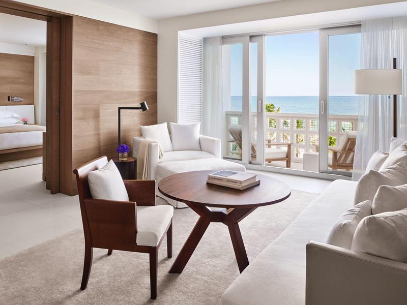 Helles Wohnzimmer mit weißen Möbeln, rundem Holztisch und großer Glasfront mit Meerblick.