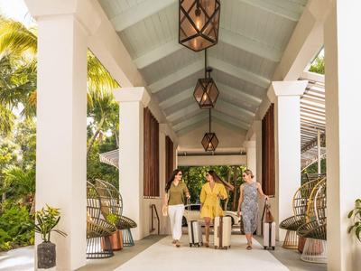 Überdachter Terrassengang mit weißen Säulen, Laternen und Pflanzen, drei Personen am Tisch.