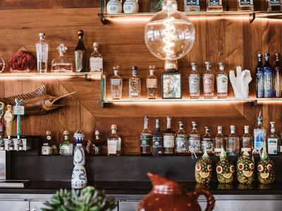 Bar mit Holzregalen voller verschiedener Spirituosenflaschen und Bierhähnen unter hellem Leuchtmittel.