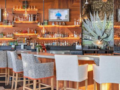 Moderne Bar mit Holzregalen, Stühlen mit Stoffbezug und eleganter Beleuchtung.